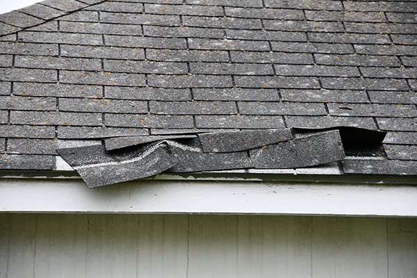 close up image of a residential roof where shingles are damaged and falling off from storm damage