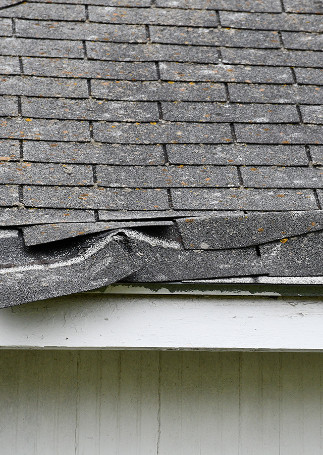 Close of image of a roof of a house where the shingles on the roof are damaged from a storm