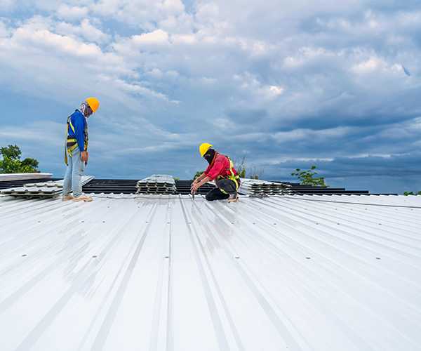 image of two commercial roofing contractors on top of a flat meta commercial roof inspecting one of the panels.