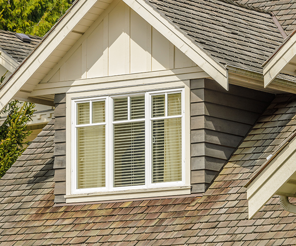 Image of a house's roof where you can see the shingles are damaged underneath the window