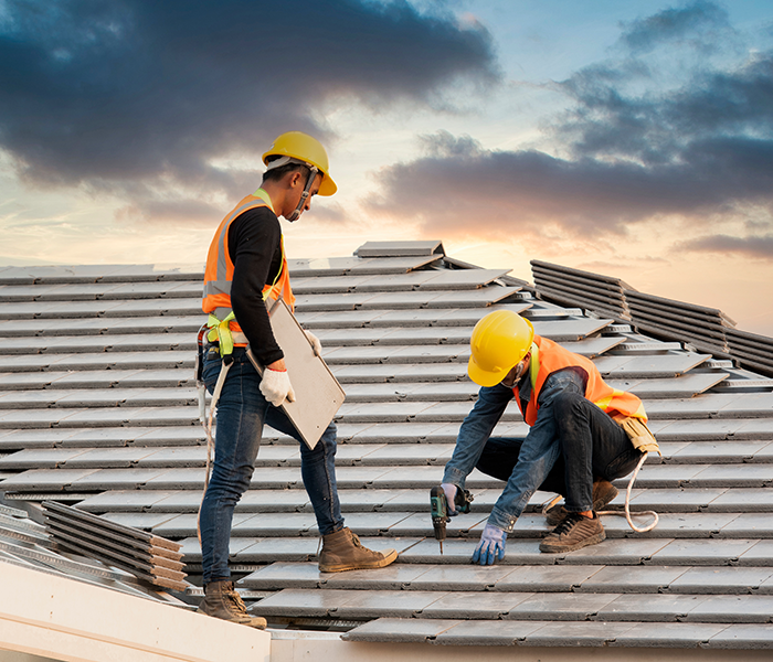 two roofing contractors on a residential roof with hard hats and construction vest